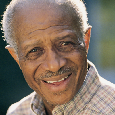 Older man smiling warmly outdoors in natural light.