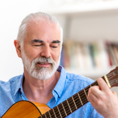 Older man playing an acoustic guitar indoors in a quiet moment.