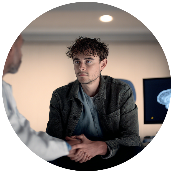 A young man sits in disbelief as a doctor shares news with him