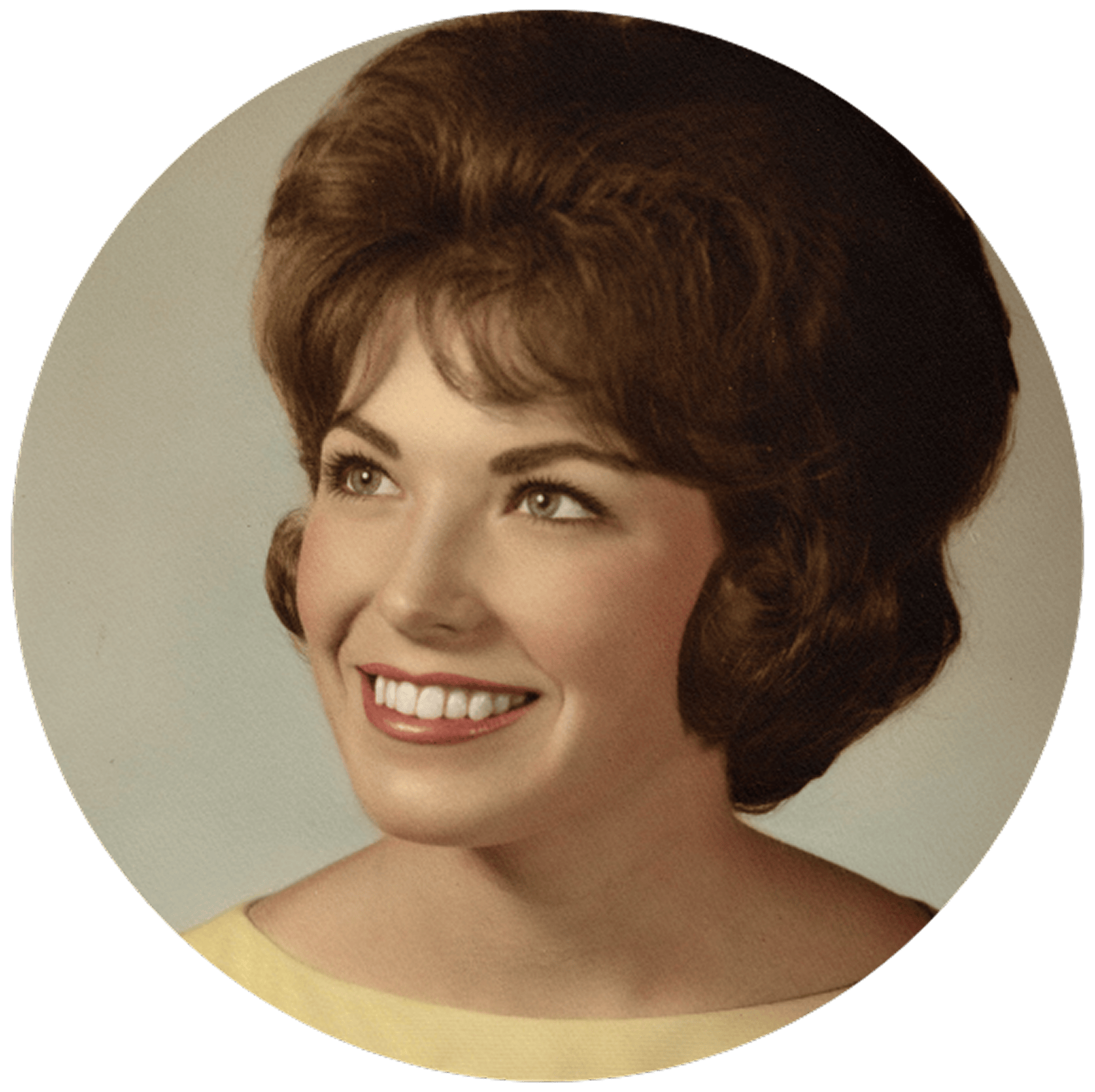 A woman with dark, styled hair smiles brightly, looking upward. She wears a light yellow top.