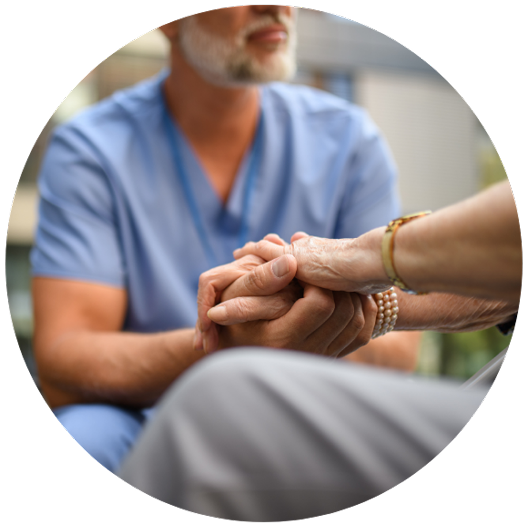 A caregiver in blue scrubs gently holds an elderly person’s hand, conveying care and compassion.