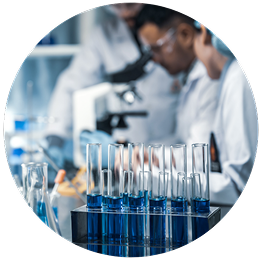 A scientist in a lab coat works with a microscope, surrounded by test tubes with blue liquid. The setting feels focused and scientific.