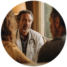 A doctor with curly hair and a stethoscope attentively listens to a couple in a warmly lit room, conveying empathy and understanding.