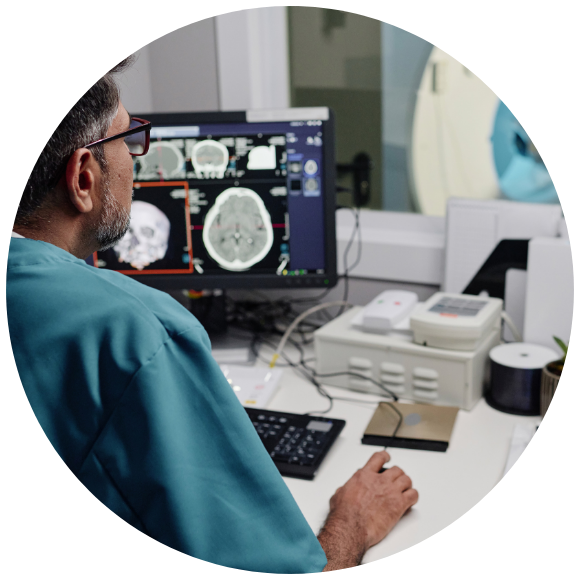 A medical professional in scrubs examines brain scans on a computer in a modern clinic. The scene conveys focus and a clinical atmosphere.