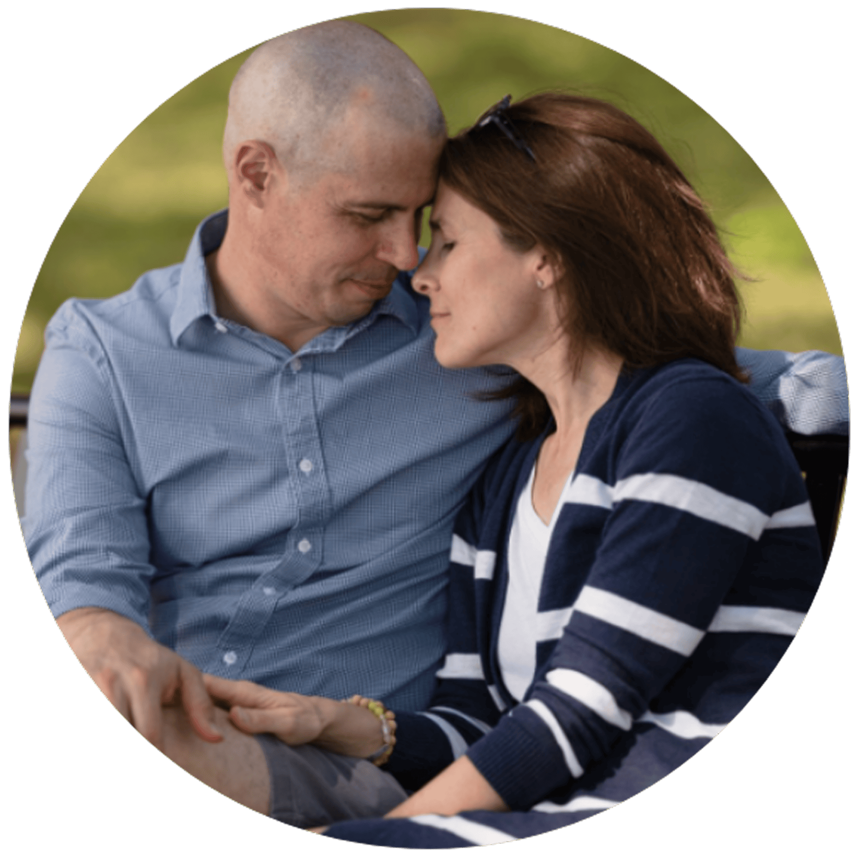 A couple sits closely on a bench, touching foreheads with eyes closed, conveying a sense of love and tranquility.