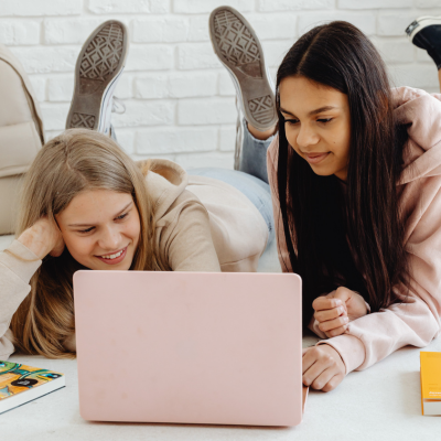 Two young people lying on the floor together, looking at a laptop screen.