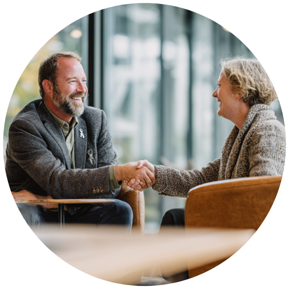 Two adults shaking hands during a supportive conversation in a comfortable indoor setting.