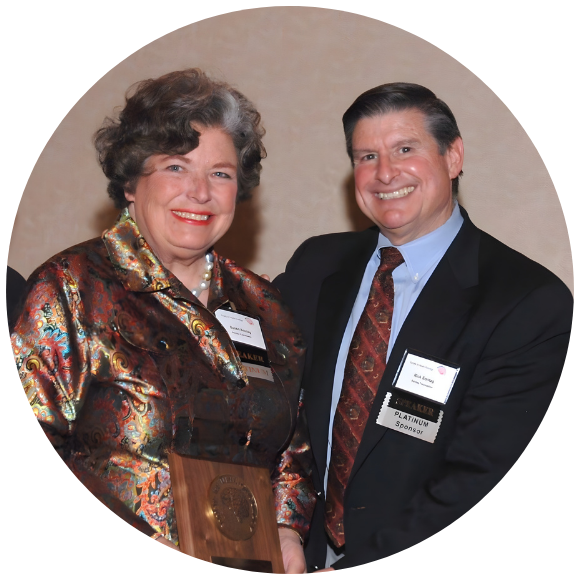 Two individuals smiling while holding an award at a formal event.