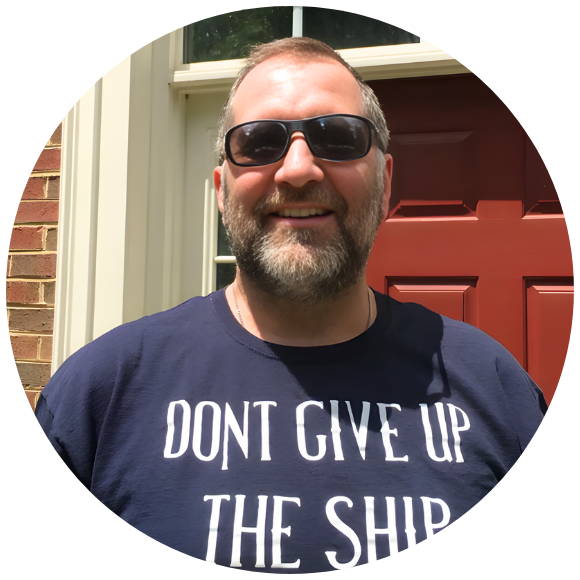 Adult man smiling outdoors while wearing sunglasses in front of his home.