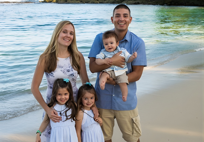 Family with three children standing together on a beach, smiling at the camera.