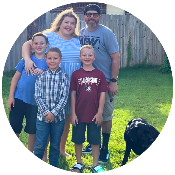 Family of five standing together outdoors in a backyard, smiling at the camera.