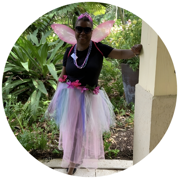Woman wearing fairy wings and a colorful tutu, smiling outdoors.