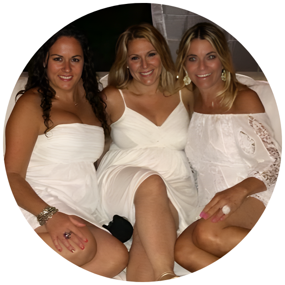 Three women sitting together, smiling and dressed in white at a social gathering.