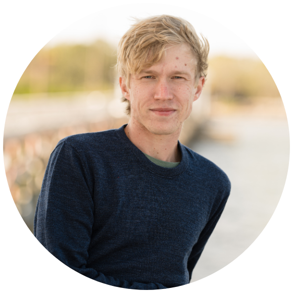 Young adult man standing outdoors near water, looking at the camera.