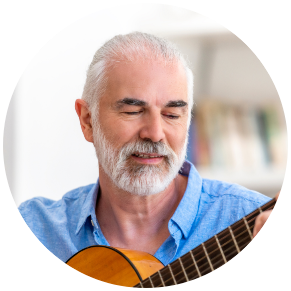 Older man playing an acoustic guitar indoors in a quiet moment.