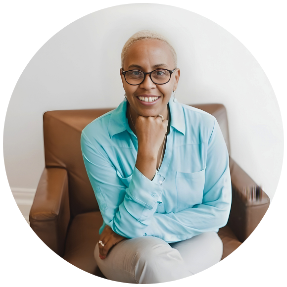 Woman with short hair and glasses smiling while seated indoors.