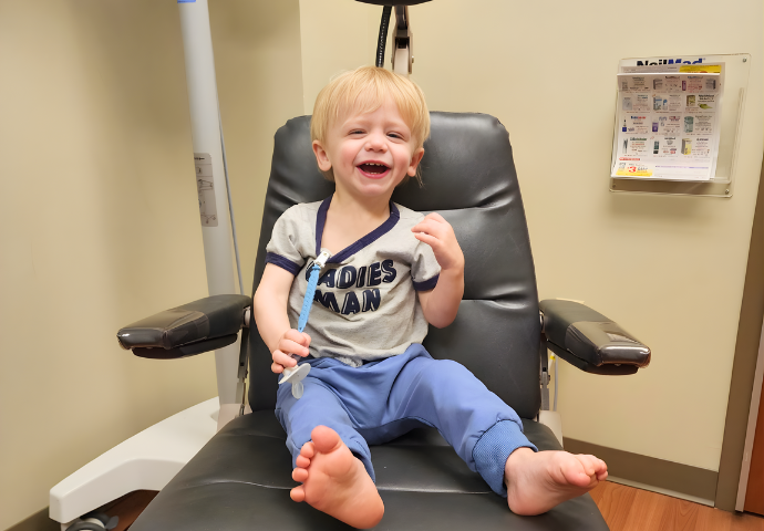 Smiling toddler sitting in a medical chair during a pediatric appointment.