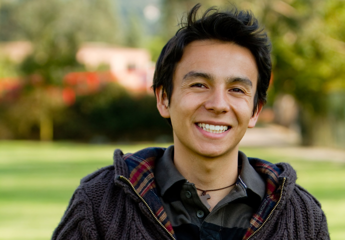 Young adult smiling outdoors in a park setting.