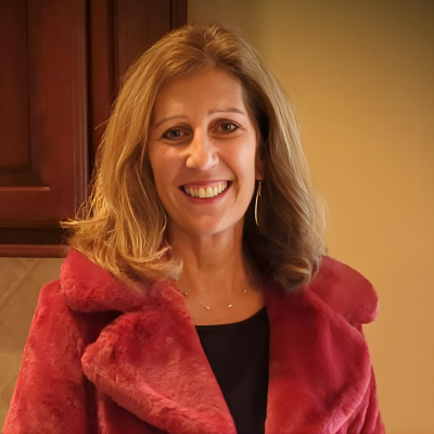 Woman smiling indoors, wearing a red jacket in a warm portrait.