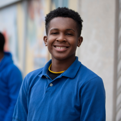Teen smiling outdoors, wearing a blue shirt and standing casually.