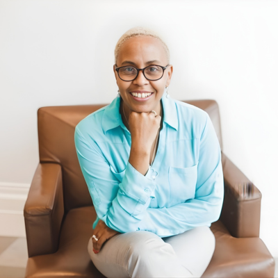 Woman with short hair and glasses smiling while seated indoors.