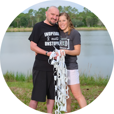 Couple standing together outdoors by a lake, holding a paper chain.
