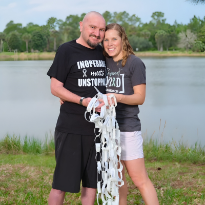 Couple standing together outdoors by a lake, holding a paper chain.