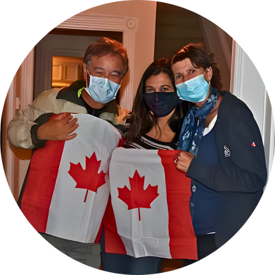 Three people wearing masks hold Canadian flags together indoors.