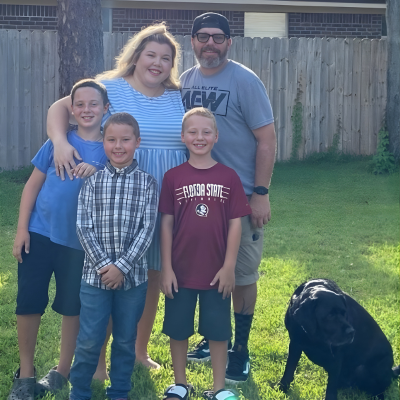 Family of five standing together outdoors in a backyard, smiling at the camera.