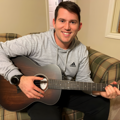 Young man smiling while playing an acoustic guitar indoors.Personal passions remain an important part of life during care.