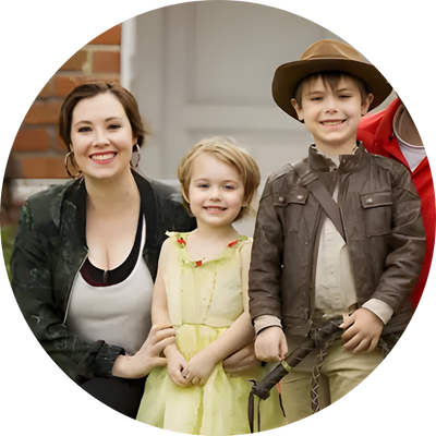 Family smiling with two young children standing together outdoors.