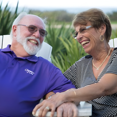 Older couple laughing together outdoors, sharing a relaxed moment.