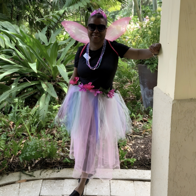 Woman wearing fairy wings and a colorful tutu, smiling outdoors.