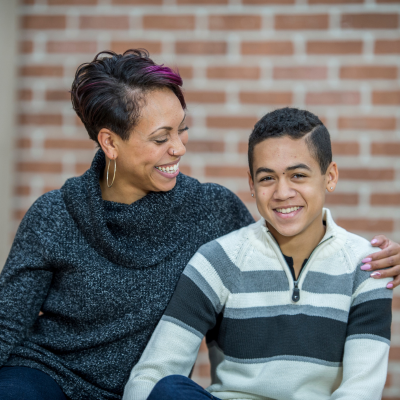 Two people sitting together outdoors, smiling and sharing a supportive moment.