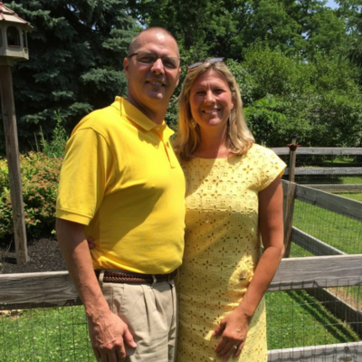 Couple standing together outdoors, smiling in a sunny setting.