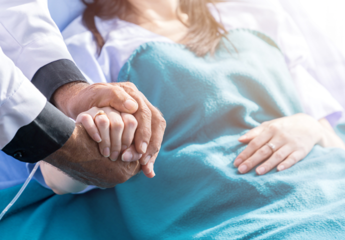 a female patient lying in bed a doctor at her side holding her hand