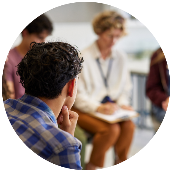a man sitting in the forefront looking at a speaker at a support group blurred in the background