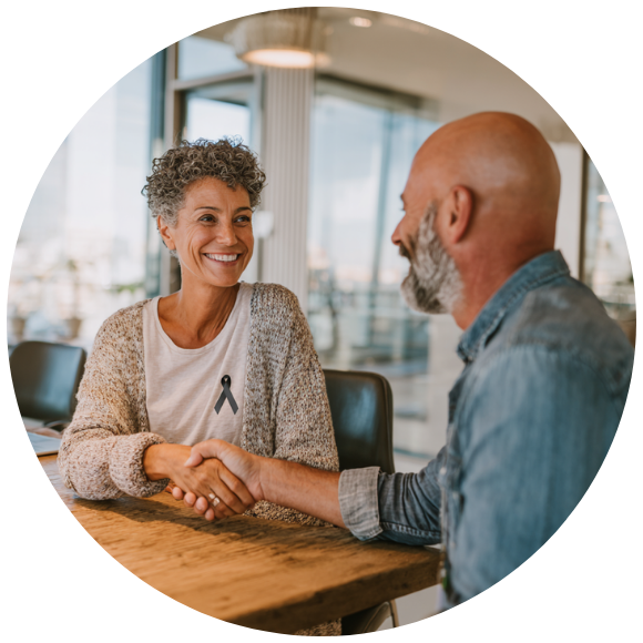 an older woman wearing a grey cancer ribbon on her shirt shakes hands with an older gentleman, smiling